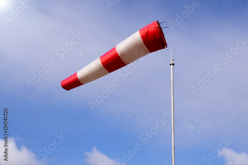 Airport windsock on clear blue sky background in windy weather indicate the local wind direction (also called: air sock, drogue, wind sleeve, wind cone). Red white striped windsock against blue sky