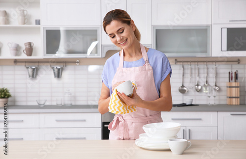 Woman wiping ceramic cup at table with clean dishes in kitchen