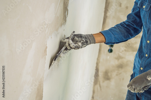 master is applying white putty on a wall and smearing by putty knife in a room of renovating house in daytime