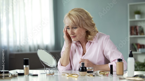 Mature lady looking with disgust at her sagging skin and wrinkles, aging process