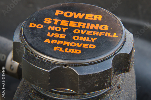 Closeup of a cap of a power steering oil tank. Do not overfill and use approved fluid only warning text.