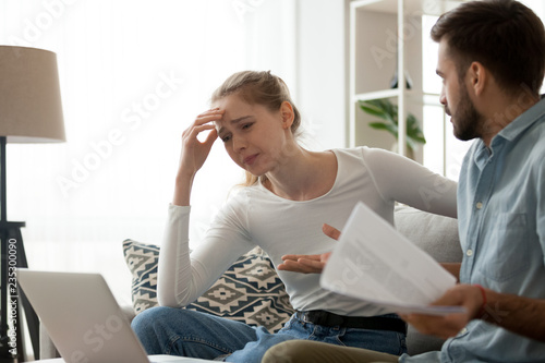 Millennial couple have fight over documents at home, man and woman sit on couch upset about bad news in letter, frustrated wife cry reading negative notice from bank, spouses dispute over bills