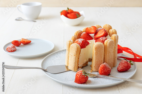 Charlotte, French dessert with strawberries, tied up with a scarlet ribbon, coffee cup, bowl with strawberries on white table.