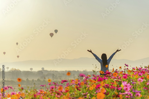 Lifestyle traveler women raise hand feeling good relax and happy freedom and see the fire balloon on the nature tea and cosmos farm in the sunrise morning. Travel and summer Concept