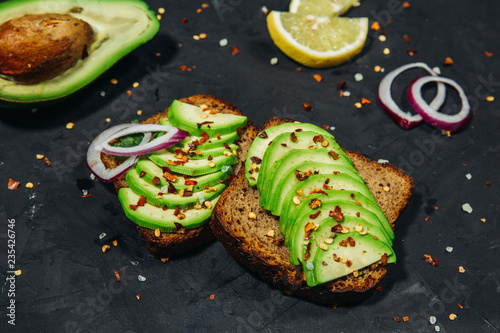 Sandwiches with avocado and spices on a black stone background, top view