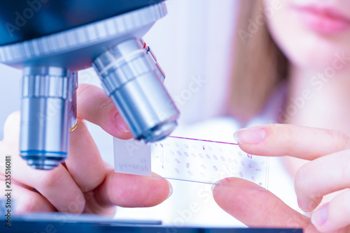 Young woman technician is examining a histological sample, a biopsy in the laboratory of cancer research