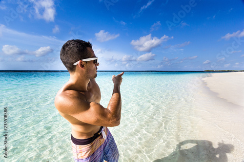 Junger Mann mit starken Armen zeigt den Weg mit dem Finger an einem traumhaften Strand auf den Malediven