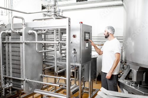 Worker operating pasteurizer using the control panel at the cheese or milk manufacturing