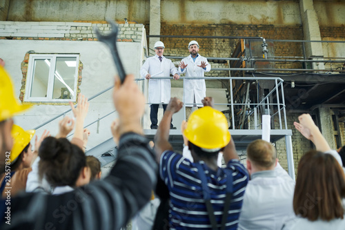 Rear view portrait of multi-ethnic group of workers protesting looking at two factory managers standing at balcony, copy space