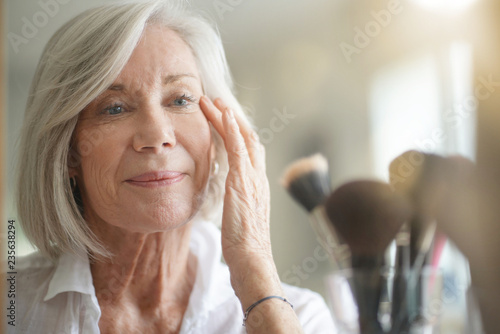 Attractive senior woman looking at herself in mirror