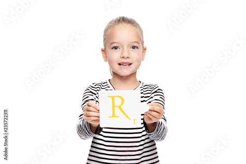 Young girl holding a card with letter R. Speech therapy concept on white background. Correct pronounciation and articulation at preschool age.