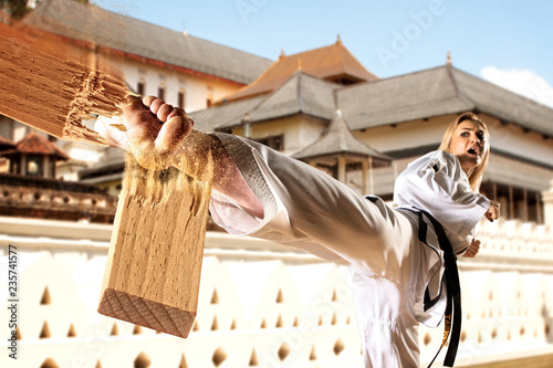 Female in kimono practicing taekwondo. Breaking board