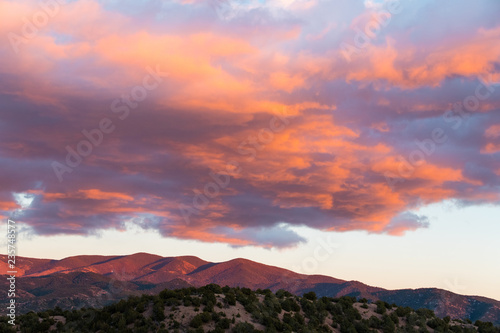 Dramatic, beautiful sunset casts purple and orange colors on clouds and the Sangre de Cristo mountains near Santa Fe, New Mexico