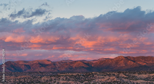 Dramatic, beautiful sunset casts purple and orange colors and hues on clouds and mountains over a neighborhood in Tesuque, near Santa Fe, New Mexico