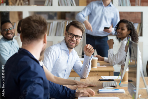 Multiracial work team having fun and laughing together, employees working and discussing about funny news in shared workspace, teamwork, good relationships in team, friendship concept