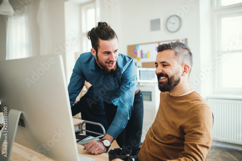 Two young male businesspeople with computer talking in a modern office.