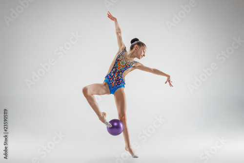 The teen female little girl doing gymnastics exercises with ball on a gray studio background. The gymnastic, stretch, fitness, lifestyle, training, sport concept