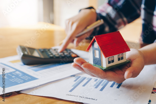 Woman holding house model in hand and calculating financial chart for investment to buying property.