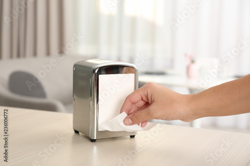 Woman taking paper tissue from napkin holder on table