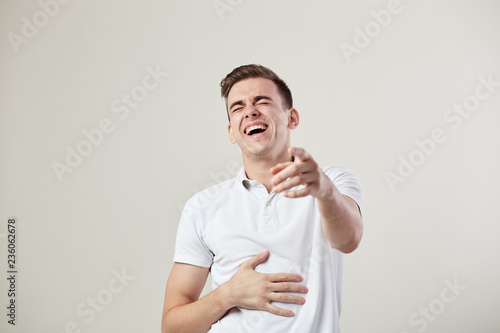 Guy dressed in a white t-shirt and jeans laughs and keeps hand on the belly on a white background in the studio