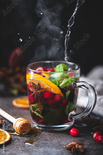Hot fruit tea with spices, orange peel and mint. Steaming glass cup of hot tea, mulled wine with cranberries or spicy cranberry grog