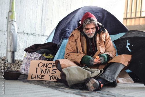 Homeless beggar man sitting outdoors in city asking for money donation.