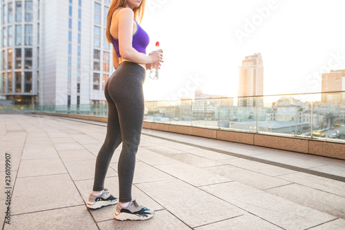 Sexy sports girl in the sunset. Sports girl with beautiful legs in leggings and a bottle of water in her hands.Girl with a beautiful bottom doing sports on the background of a beautiful city landscape
