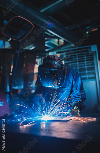 london, england, 02/02/2018 A vibrant action shot of a skilled working metal welder in action, welding metal. Photographed with a slow shutter speed and spark trails. Orange and teal.