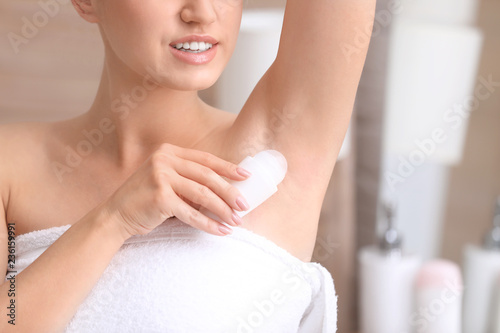 Beautiful young woman applying deodorant after shower in bathroom