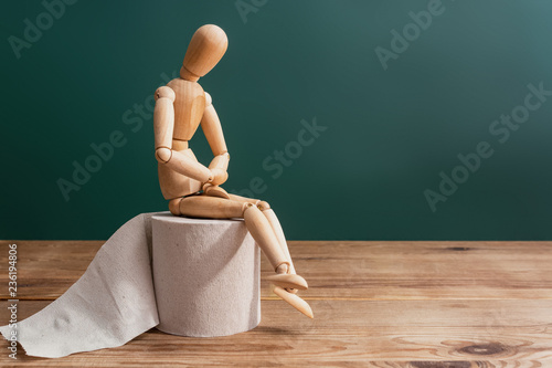 Wooden figure sit on a roll of toilet paper. Concept of the problem with digestion.