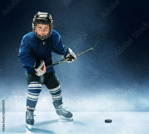Little boy playing ice hockey at arena. A hockey player in uniform with equipment over a blue background. The athlete, child, sport, action concept