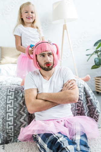 adorable happy daughter playing with father in pink wig and tutu skirt