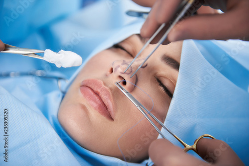 Close up photo of lady with nice lips in operating room. Doctor in gloves holding medical instrument during rhinoplasty