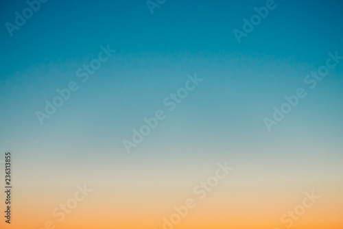 Predawn clear sky with orange horizon and blue atmosphere. Smooth orange blue gradient of dawn sky. Background of beginning of day. Heaven at early morning with copy space. Sunset, sunrise backdrop.