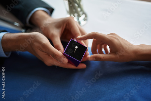Concept of romantic engagement. Close up portrait of young male holding box with expensive beautiful ring and making marriage proposal to his lady