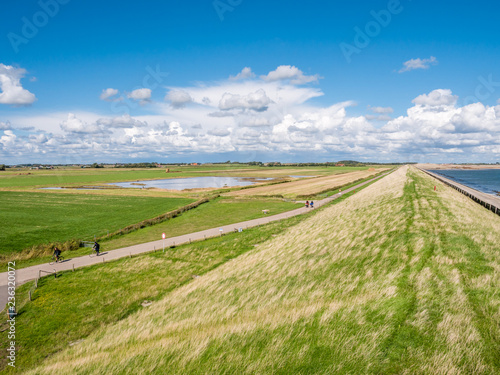 People riding bikes on small road between polder and sea dike on West Frisian island Texel, Netherlands