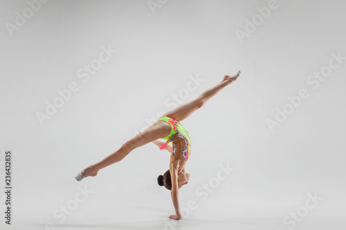 The teen female little girl doing gymnastics exercises isolated on a gray studio background. The gymnastic, stretch, fitness, lifestyle, training, sport concept