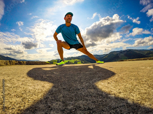 Male athlete runner stretching outdoors at sun and blue sky background. Side lunge stretch.