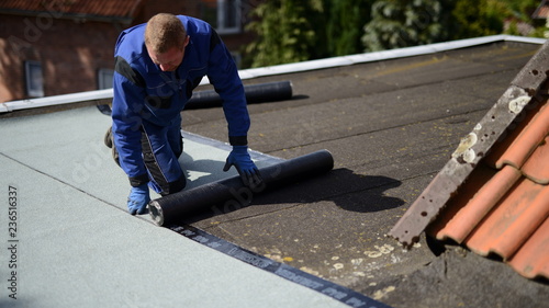 Dachdecker Facharbeiter auf Flachdach Baustelle mit Bitumen Dachpappe Baumaterial beim Abkleben vom Hallendach Haus