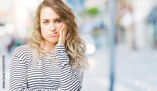 Beautiful young blonde woman wearing stripes sweater over isolated background thinking looking tired and bored with depression problems with crossed arms.