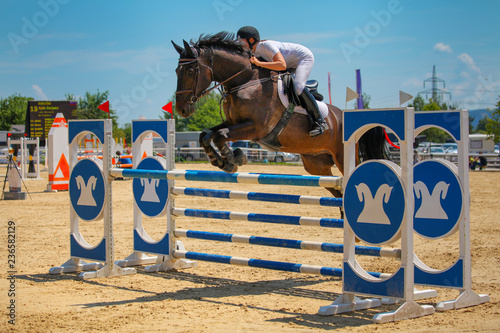 Girl riding her horse and jumping over the colorful obstacle during competition
