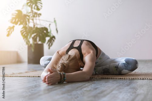 Close-up attractive sporty young woman practicing yoga indoor on wooden floor on bamboo mat. Beautiful fitness girl doing yoga asana in class. Healthy lifestyle, calmness, relax