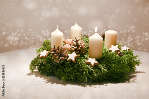 First Advent - decorated Advent wreath from fir and evergreen branches with white burning candles, tradition in the time before Christmas, warm background with festive bokeh and copy space