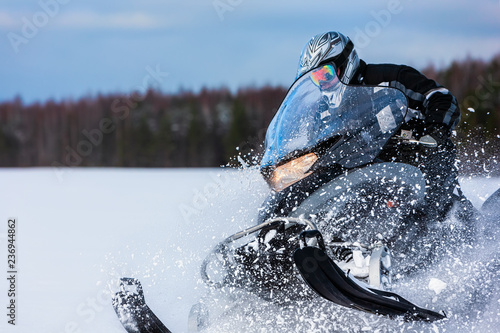 In deep snowdrift snowmobile rider driving fast. Riding with fun in white snow powder during backcountry tour. Extreme sport adventure, outdoor activity during winter holiday on ski mountain resort.