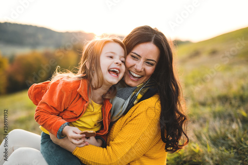 A portrait of young mother with a small daughter in autumn nature at sunset.