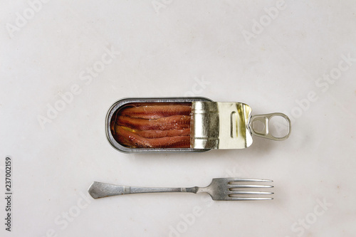 Pickled salted anchovies fillet in oil in open tin can with fork over white marble background. Flat lay, copy space