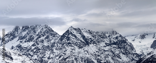 Panoramic view on snowy rocky mountains and cloudy gray sky