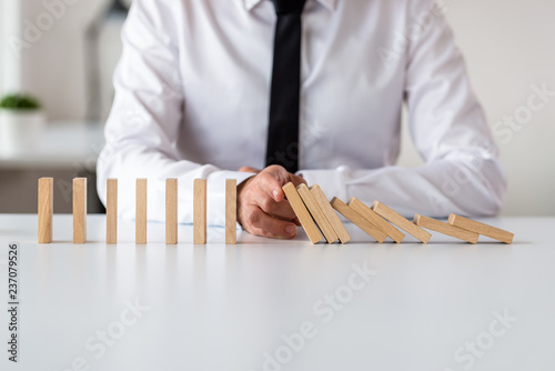 Business executive sitting at his office desk stopping domino effect