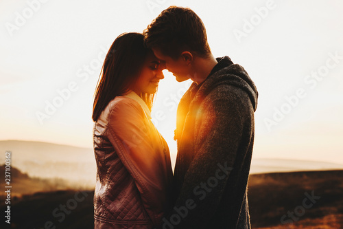 Side view of attractive young man and woman standing against sunset sky in wonderful countryside.Cute couple against sundown sky