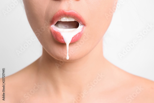 Young woman with white liquid dripping from her mouth on light background. Erotic concept